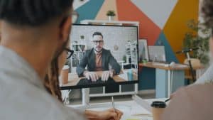 Team engaging in a video conference call with a colleague on screen in a modern office, representing AI meeting transcription tools