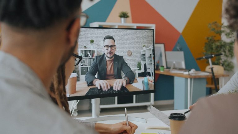Team engaging in a video conference call with a colleague on screen in a modern office, representing AI meeting transcription tools