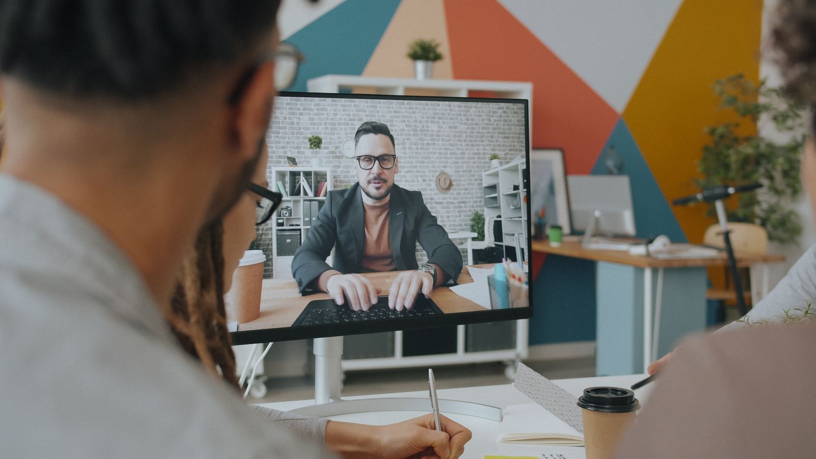 Hands at a laptop showing a group video call in a home office setting, representing AI meeting transcription tools