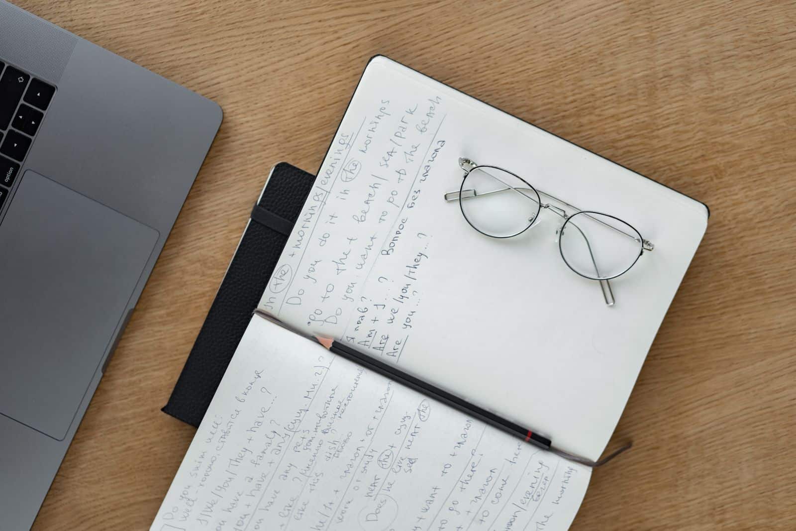 Close-up of a woman writing notes in a notebook beside a laptop on a wooden desk, representing Granola AI notes