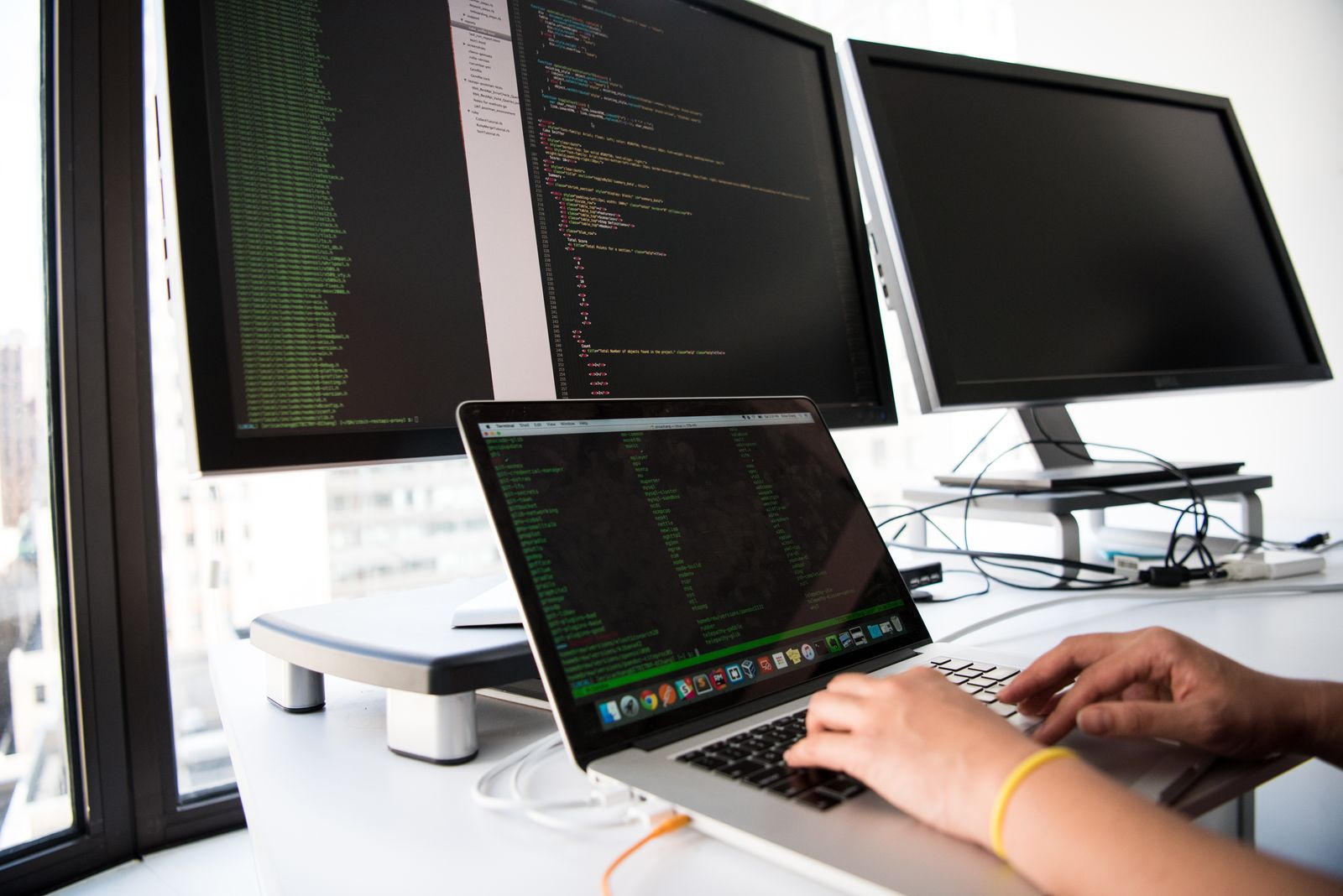 Developer working on a laptop in front of multiple monitors, representing building and testing automation workflows
