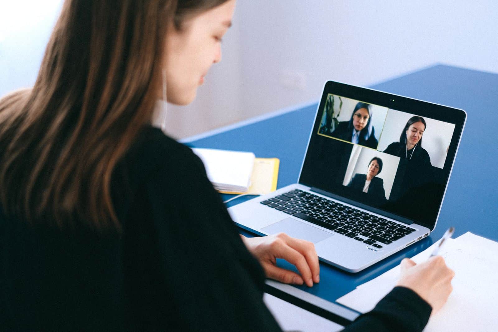 Woman engaging in a video conference using a laptop at home while taking notes, representing Otter.ai